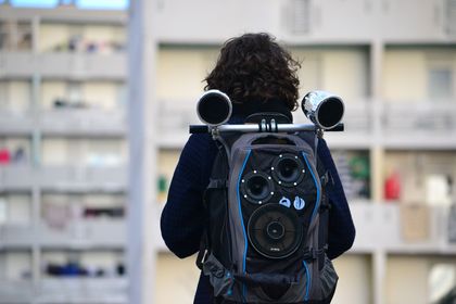Fanny Ohier (de dos) porte un sac à dos transformé en enceinte devant une tour de Frais Vallon