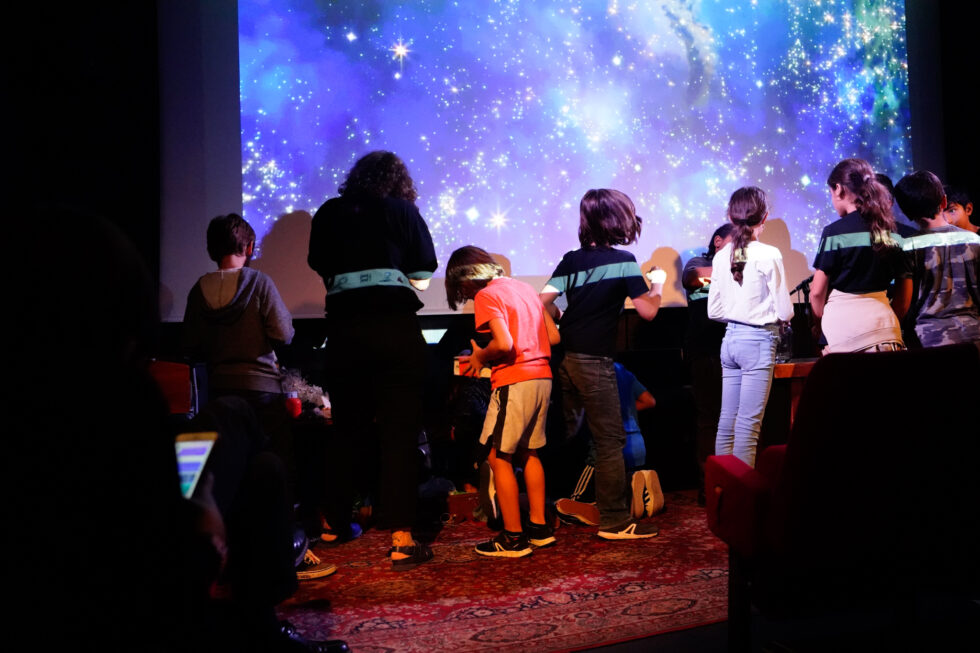 Samia et des enfants devant la projection d'étoiles dans un cinéma fouillent dans des malettes de bruitage