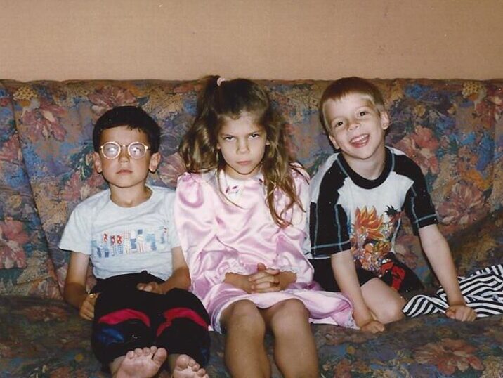 Samia est assise sur un canapé entre deux autres enfants. Elle n'a pas l'air très sympathique, contrairement aux deux autres.