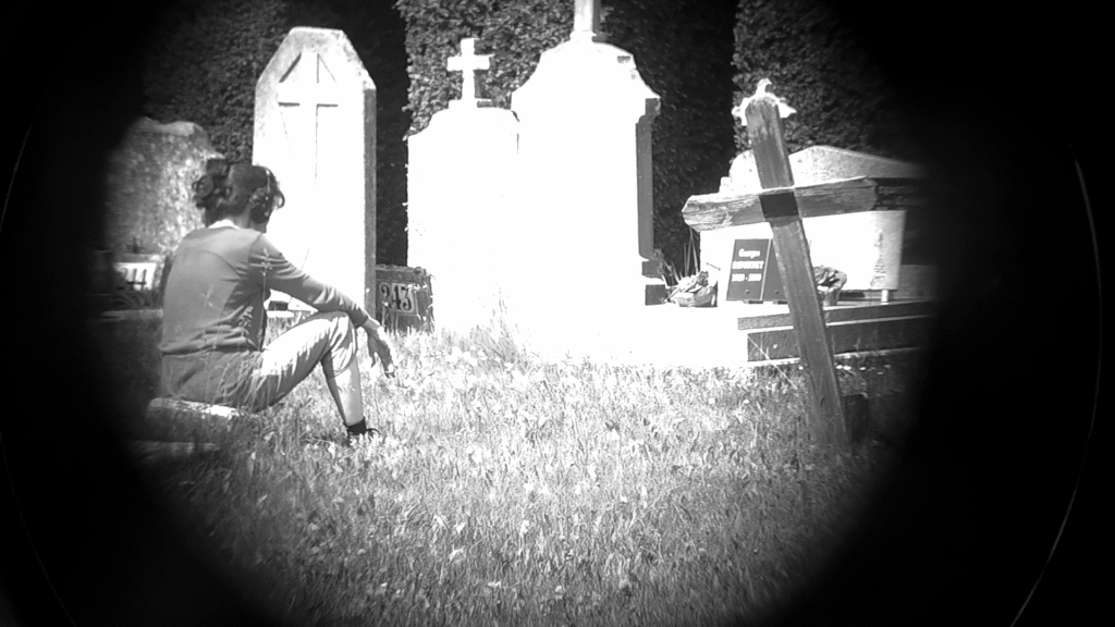 Une femme, un casque sur les oreilles, assise dans l'herbe face à une sépulture